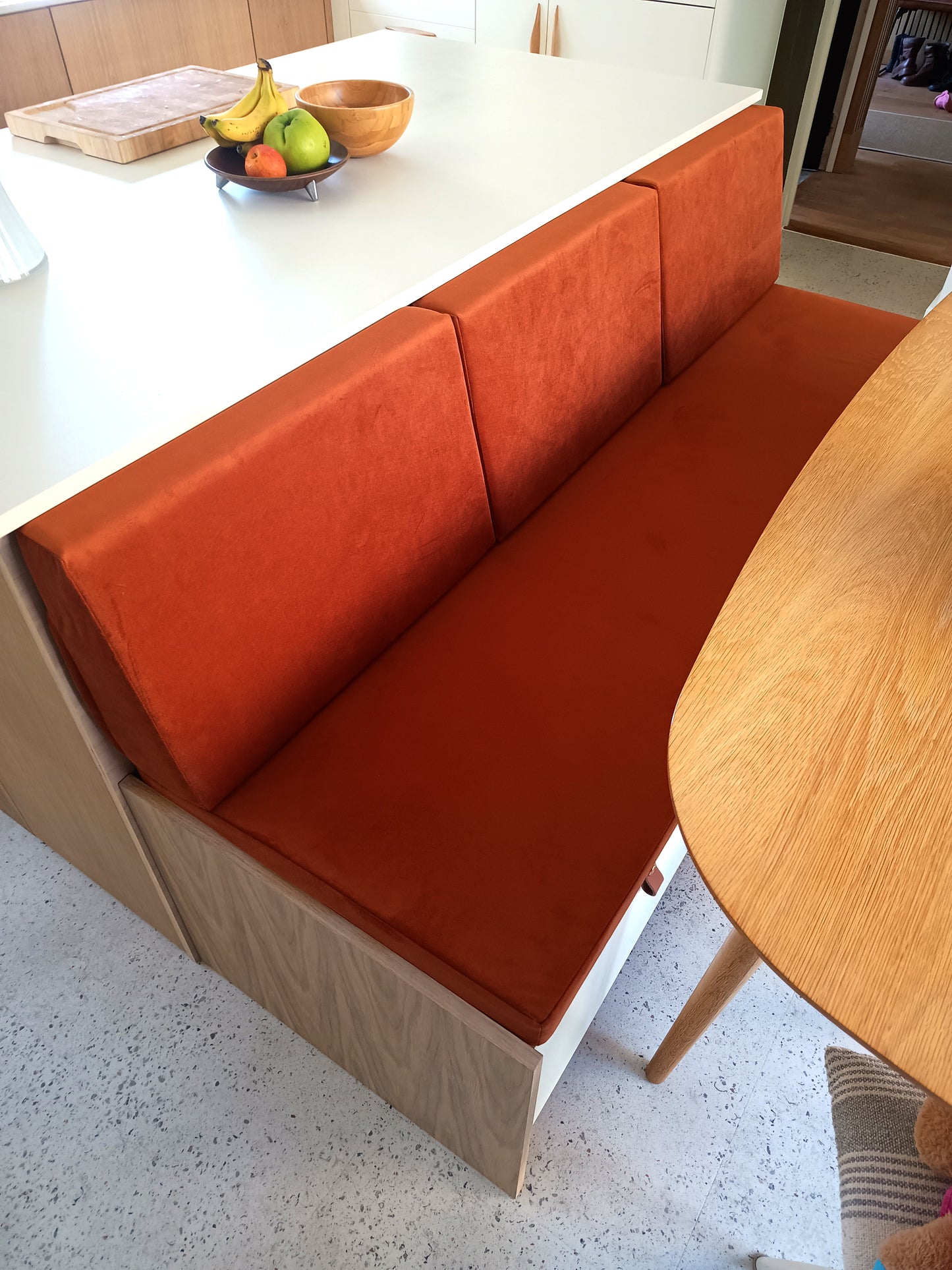 A modern kitchen diner banquette seat. Wooden built in kitchen seating with a made to measure velvet bench seat cushion in a burnt orange low pile, easy care performance velvet fabric. Bench cushion cover with stain resistant treatment, perfect for use in kitchens and dining spaces, dining booths, around children and pets. Dog friendly bench cushion seating. Back cushions for dining banquette in slanted bolster shape with high quality firm supportive foam in side. Made in UK luxury high quality.