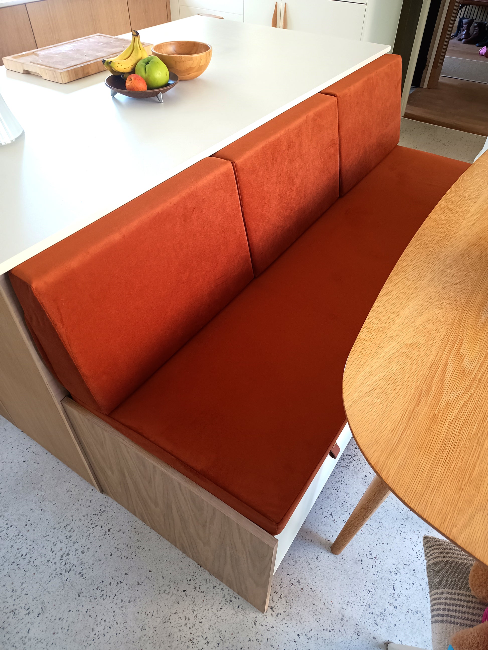 A modern kitchen diner banquette seat. Wooden built in kitchen seating with a made to measure velvet bench seat cushion in a burnt orange low pile, easy care performance velvet fabric. Bench cushion cover with stain resistant treatment, perfect for use in kitchens and dining spaces, dining booths, around children and pets. Dog friendly bench cushion seating. Back cushions for dining banquette in slanted bolster shape with high quality firm supportive foam in side. Made in UK luxury high quality.