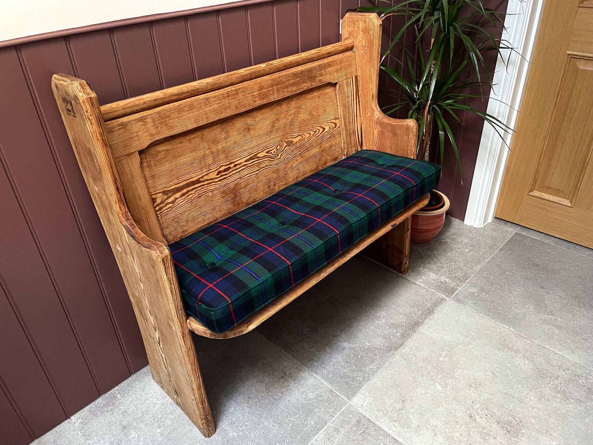 A narrow wooden church pew bench with a hand button tufted bench cushion made to measure on top. Family tartan cushions in plaid wool fabric. Buttoned and piped bench cushion for indoor bench. Navy blue, emerald green and red check patterned fabric bench cushion with firm foam and dacron wadding inside. Wipe clean natural fibre fabric bench cushion. Hard wearing and long lasting for dining bench, banquette, in built wooden seating area. Hanging bar back cushion pads with velcro and fabric ties