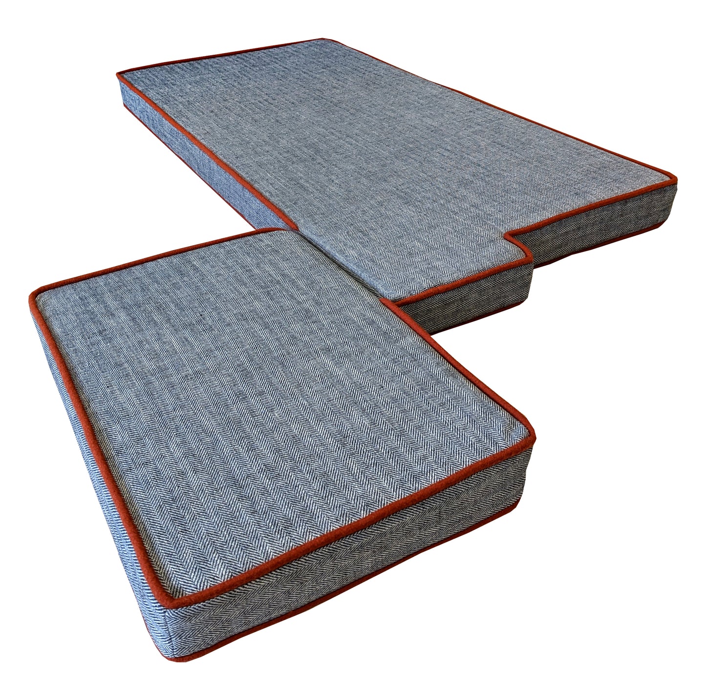 A set of two made to measure bench cushions in a dark navy blue and off white herringbone hard wearing fabric with a burnt orange wool fabric piping at the edges. The firm foam seat cushions have cut outs and odd shapes to give a good fit for the kitchen seating nook these bench cushions were made for. The long lasting wool look fabric has a geometric semi plain pattern on in a dark blue colour. The bench cushions have zips at the back of the covers and stockinette wrap on the upholstery foam