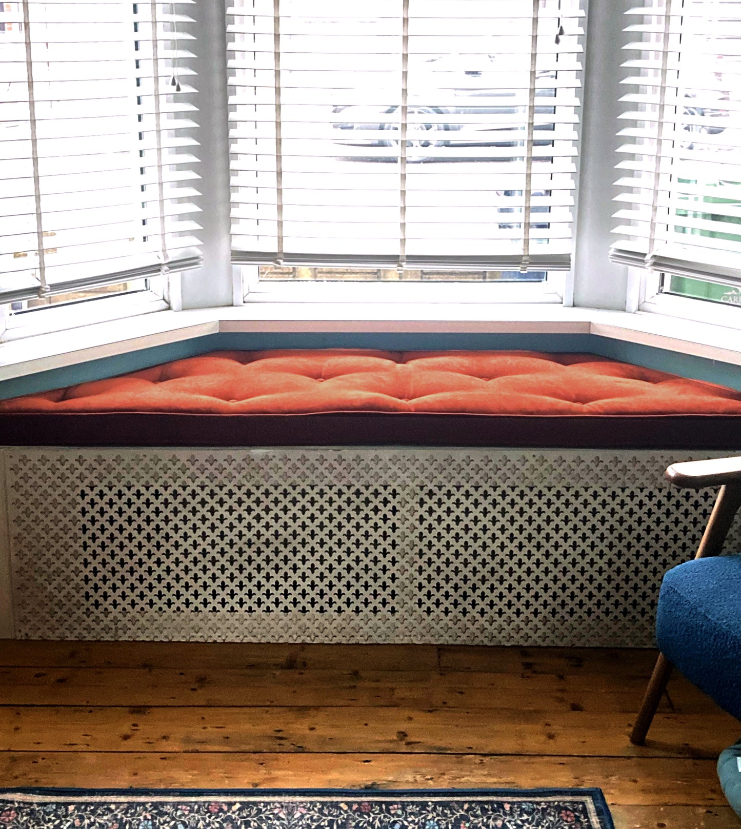 A trapezium shaped window seat cushion made to measure with slanted edge shaping. Firm foam and dacron wadding trapezoid shape bench cushion with button tufting and piped edges. Window storage ledge wooden in built radiator cover seat cushion. Dark orange chenille velvet upholstery fabric anti slip, velcro strips. Angled edge indoor bench cushion made to measure in Yorkshire UK. Orange herringbone tweed fabric bench cushion. Dining bench, kitchen banquette, shoe rack cushion, velcro straps, pets