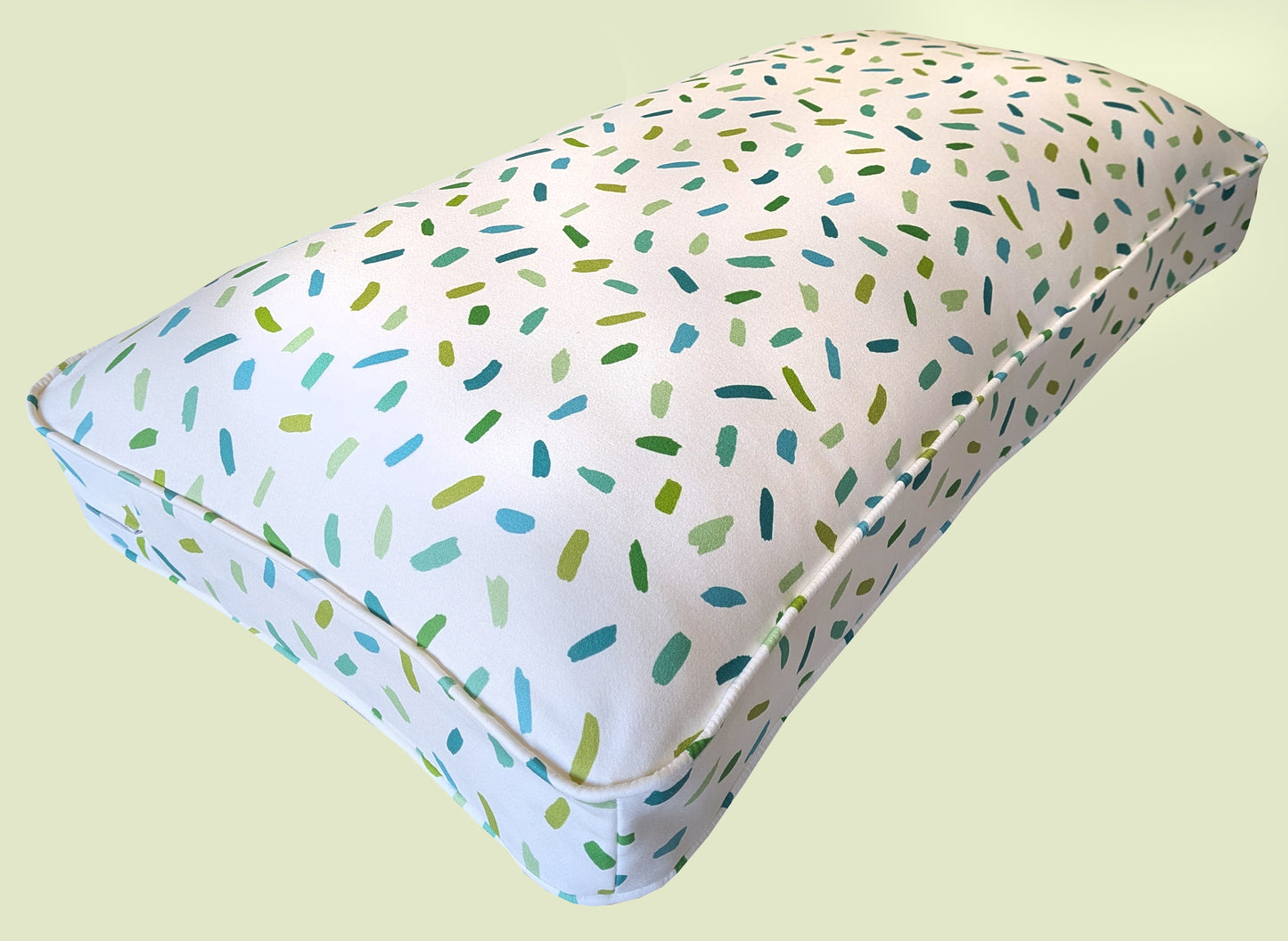 A thick, plump hollow fibre bench cushion with a natural fibre cotton bench cushion cover with a white background and green and blue confetti painted pattern. The high quality window seat cushion has a long lasting fibre filling and a zip at the back. Kids room bench cushion, bulkhead cushion. Made to measure. Uk based small business. Designer fabrics for bench cushions. Orla Kiely, Liberty, Pure Edit, Colours of Arley, William Morris, Sophie Allport. Feather and foam filling, sheep wool, hemp.