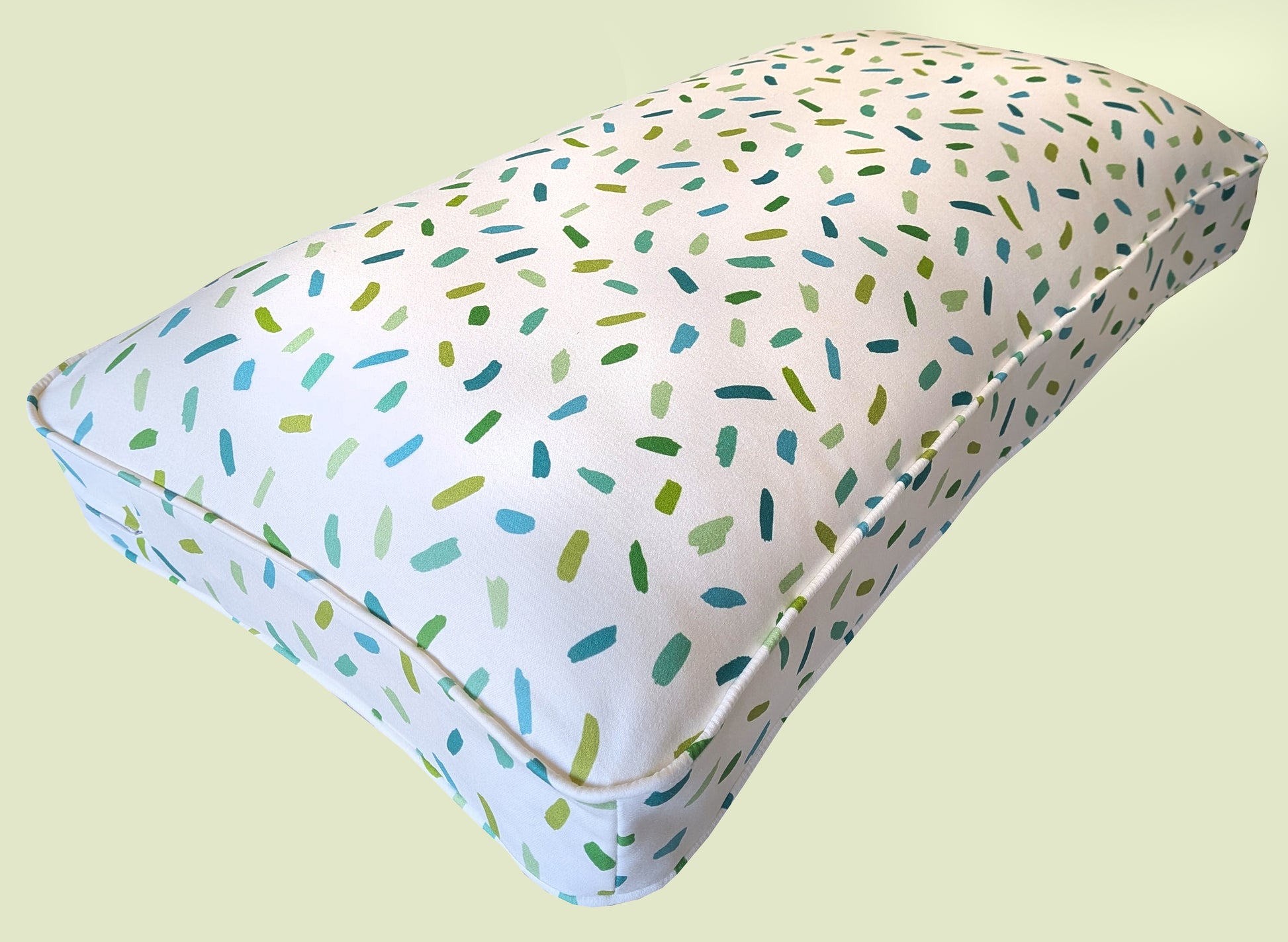 A thick, plump hollow fibre bench cushion with a natural fibre cotton bench cushion cover with a white background and green and blue confetti painted pattern. The high quality window seat cushion has a long lasting fibre filling and a zip at the back. Kids room bench cushion, bulkhead cushion. Made to measure. Uk based small business. Designer fabrics for bench cushions. Orla Kiely, Liberty, Pure Edit, Colours of Arley, William Morris, Sophie Allport. Feather and foam filling, sheep wool, hemp.