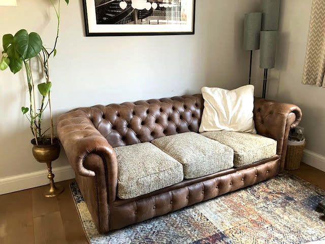 A bright living room in neutral tones with a brown leather buttoned chesterfield style sofa. Three replacement seat cushions on the sofa are covered in a multi tone beige, oatmeal coloured hardwearing boucle fabric. The sofa cushion covers have piped edges and zips at the back. The hard wearing pet friendly fabric is machine washable and long lasting. Fresh, plump hollow fibre filled sofa cushions with an eco friendly recycled plastic fibre fill. Easy care sofa seat cushions and back cushions.
